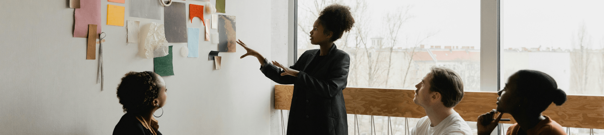 People seated at a table, actively discussing, as one points to a wall, emphasizing a talent advisory session. People seated at a table, actively discussing, as one points to a wall, emphasizing a talent advisory session.