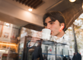 A man inside a stylish cafe sipping coffee from a styrofoam cup.